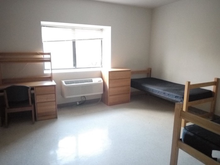 Desk with a chair, sunny window, air conditioner and two beds.
